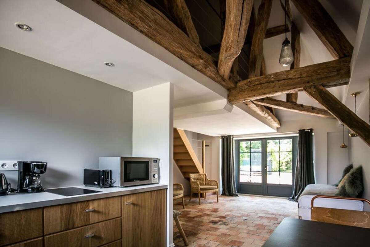Una cocina moderna con vigas de madera, un comedor con sofá y una escalera que lleva a un balcón.