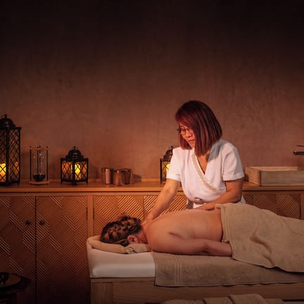 A massage therapy room with a wooden cabinet, a massage table, and several lit lanterns.