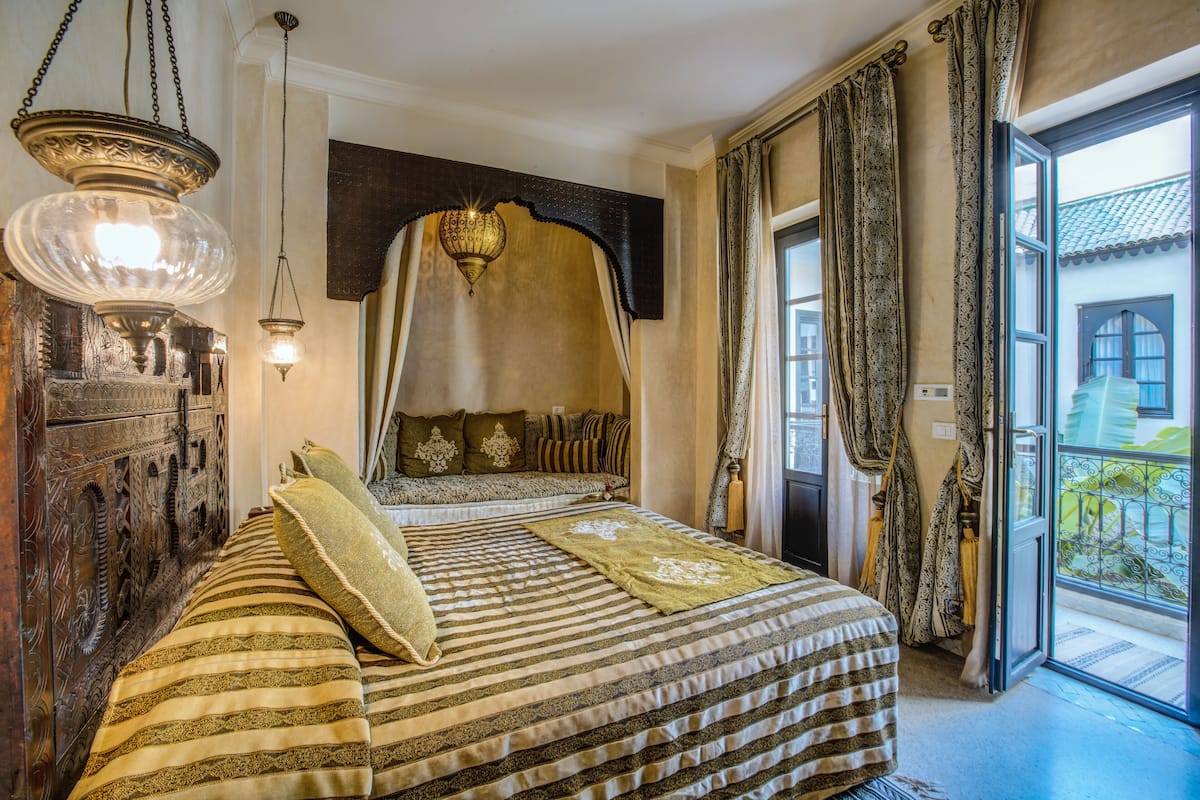 Una habitación con una cama grande, un cabecero decorado, una lámpara colgante y vistas a un balcón.