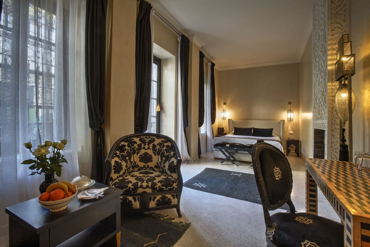 Habitación de hotel con cama, escritorio con un florero, una silla, una mesa y una chimenea.