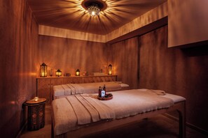 A spa room with two beds, wooden walls, and ambient lighting.