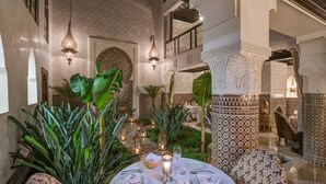A dining area with a table set for four, surrounded by lush green plants and traditional decor. - Riad Kheirredine (Marrakech)