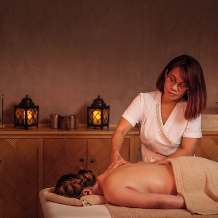 A massage therapy session in a room with wooden paneling, a wooden counter with candles, and a small table with a bottle and a bowl.