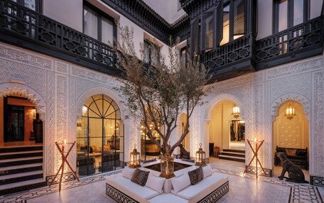 A courtyard with a central seating area, ornate walls, and a tree.