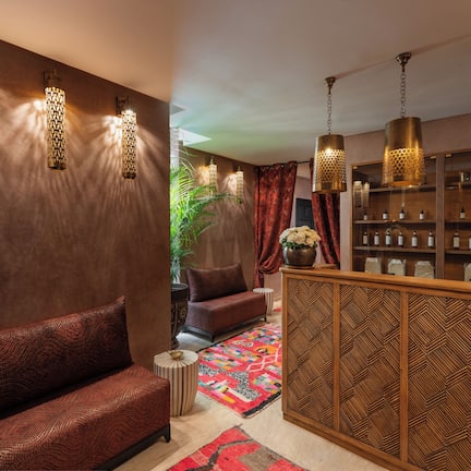 A modern interior with a sofa, patterned cushions, a patterned rug, and a wooden cabinet with bottles.