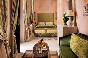 A hotel room with a bed, a green sofa, a table with a fruit bowl, and a lamp.