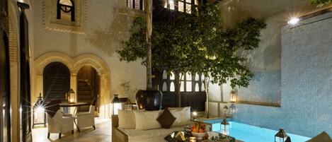 A spacious indoor area with a pool, comfortable seating, and a large tree providing shade.