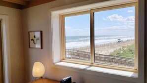 Habitación con una ventana grande que da a una playa, una obra de arte abstracta enmarcada y una lámpara sobre una mesa.