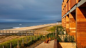 Un edificio de madera con vista a la playa, una terraza de madera y un sendero arenoso que lleva a la orilla.