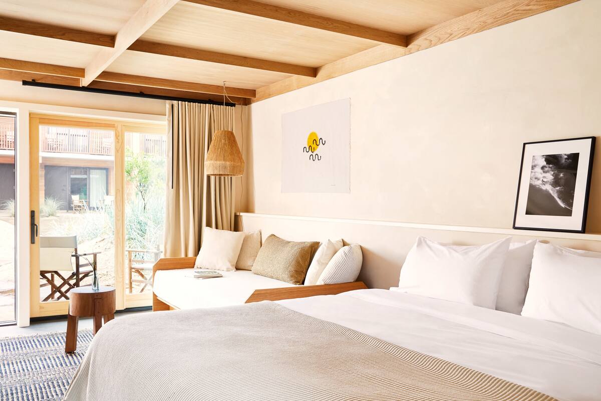A hotel room with a large bed, a small table, and a view of the outdoors.