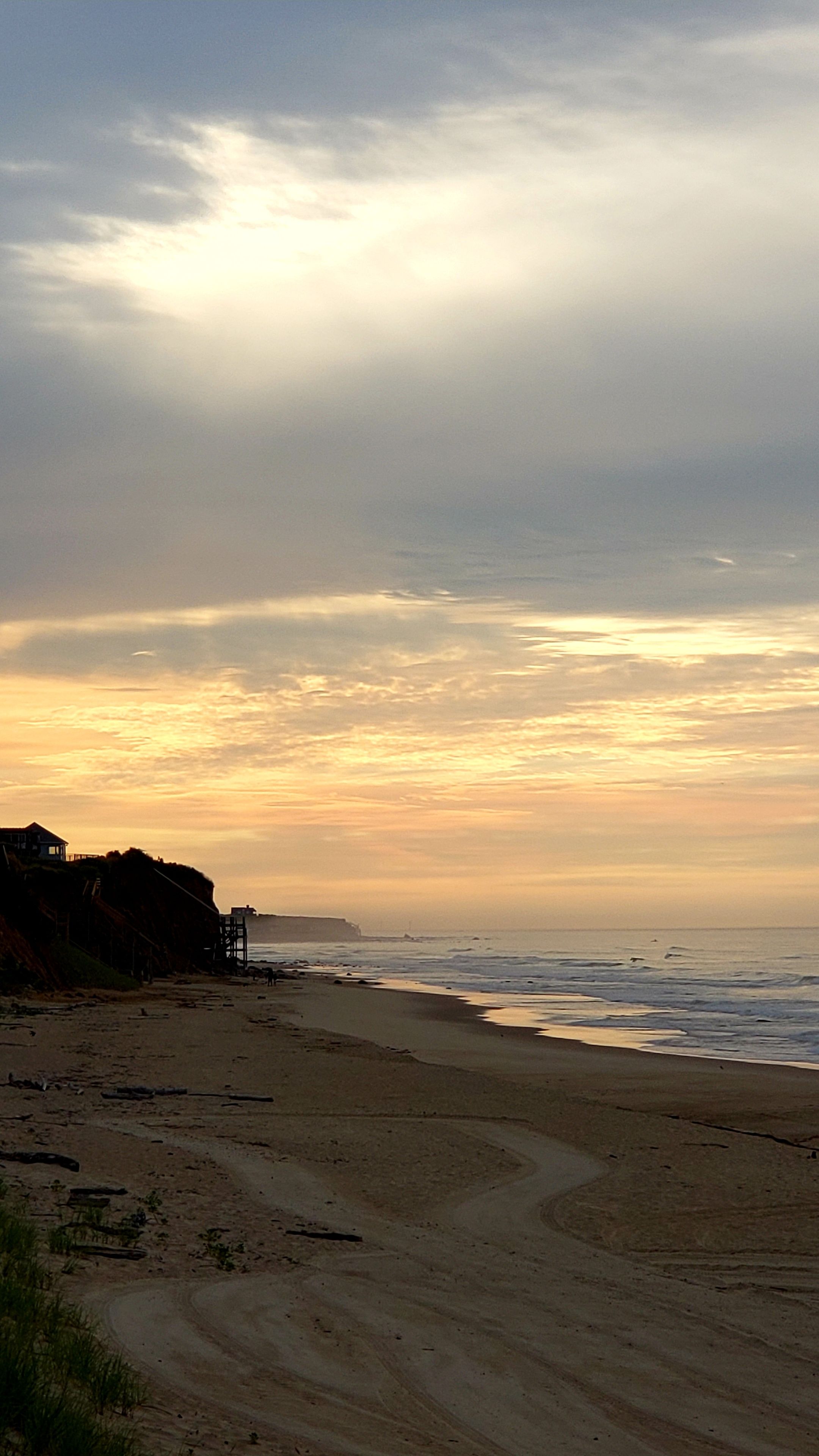 A beach with a clear sky, a structure on the left, and waves in the distance.