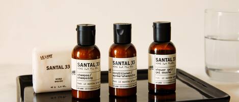 Three bottles of Santal 33 shampoo and conditioner on a tray, with a bar of soap and a glass of water.