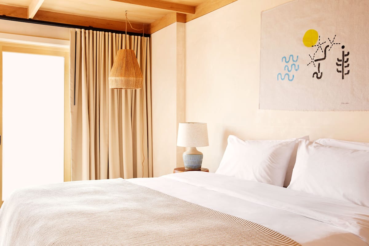 A bedroom with a bed, a lamp, curtains, and a painting on the wall.