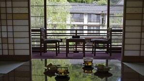 Una habitación japonesa tradicional con suelo de tatami, una mesita baja con juego de té y vistas a una zona residencial a través de amplios ventanales.