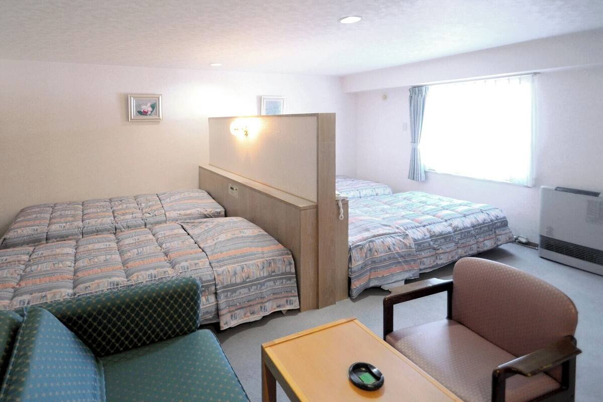 A small, well-lit room with two beds, a sofa, a chair, and a table.