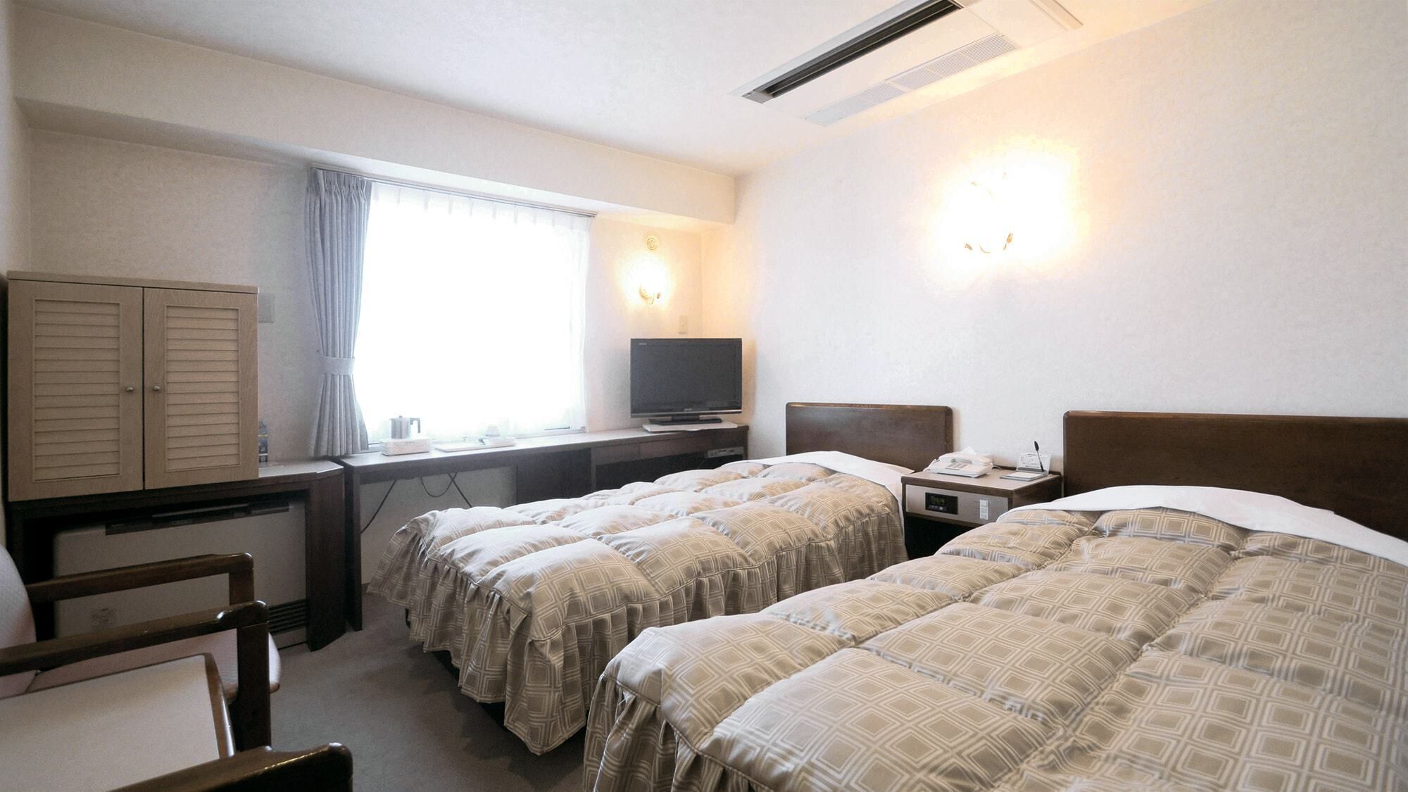 A hotel room with two beds, a desk with a television, a wardrobe, and a window with curtains.