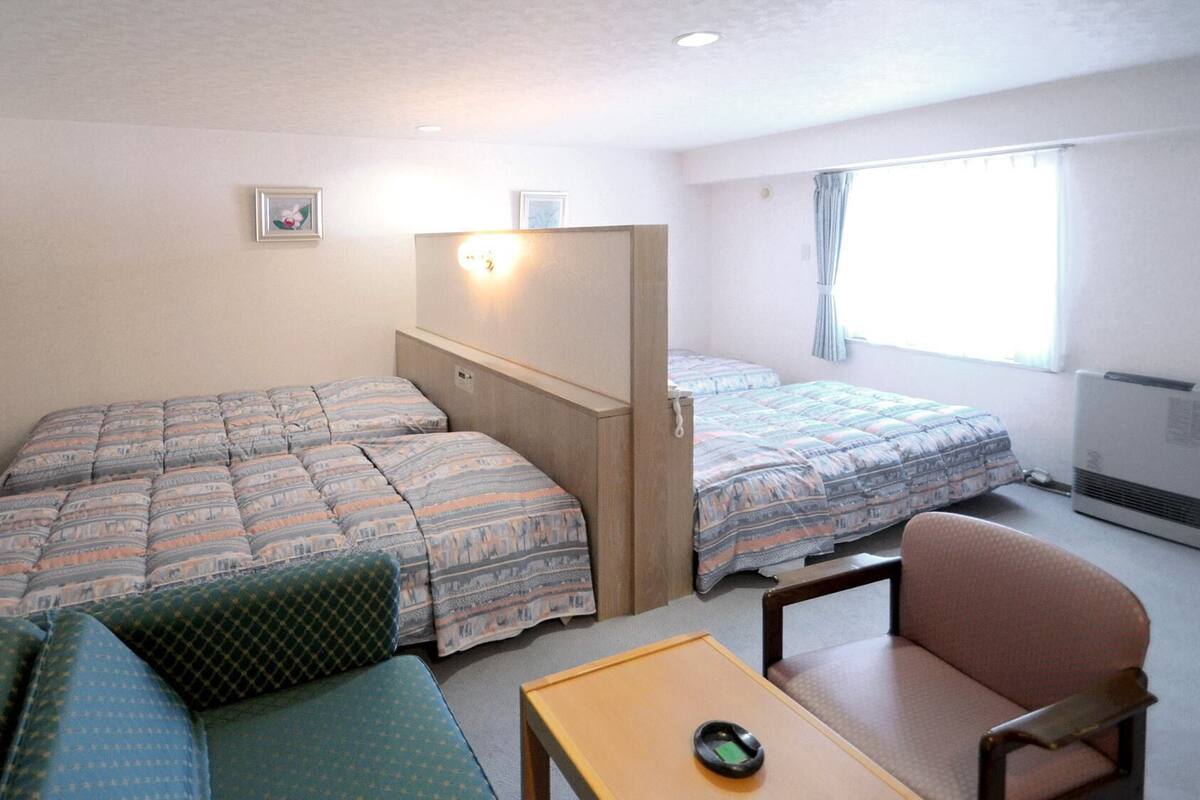 A small, well-lit room with two beds, a sofa, a chair, and a table.
