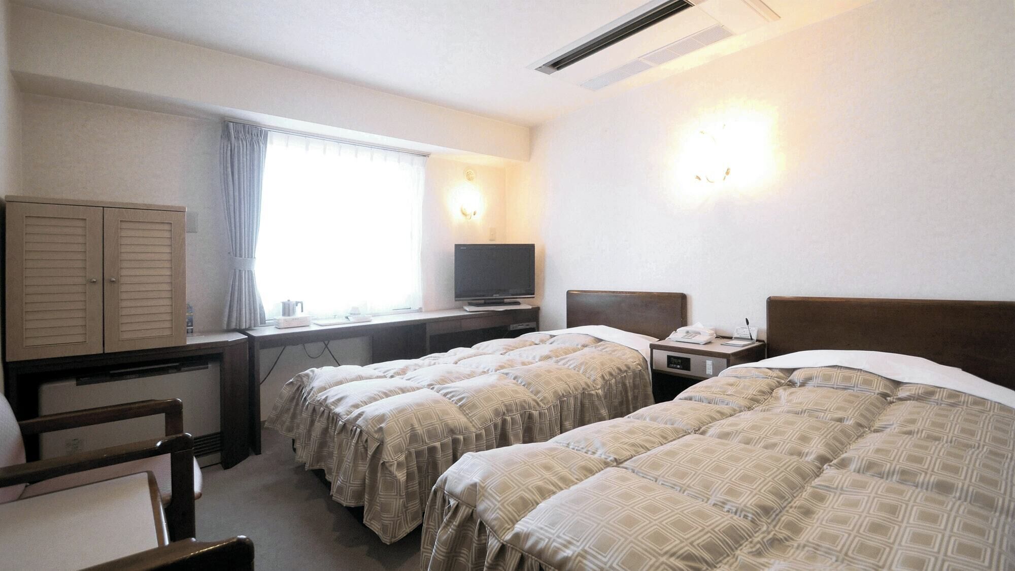 A hotel room with two beds, a desk with a television, a wardrobe, and a window with curtains.
