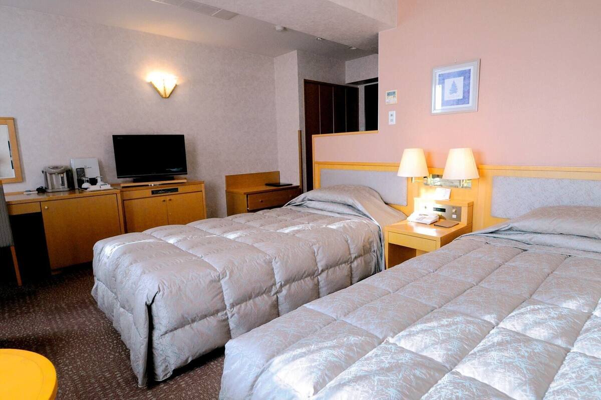 A hotel room with two beds, a desk with a TV, and a lamp.