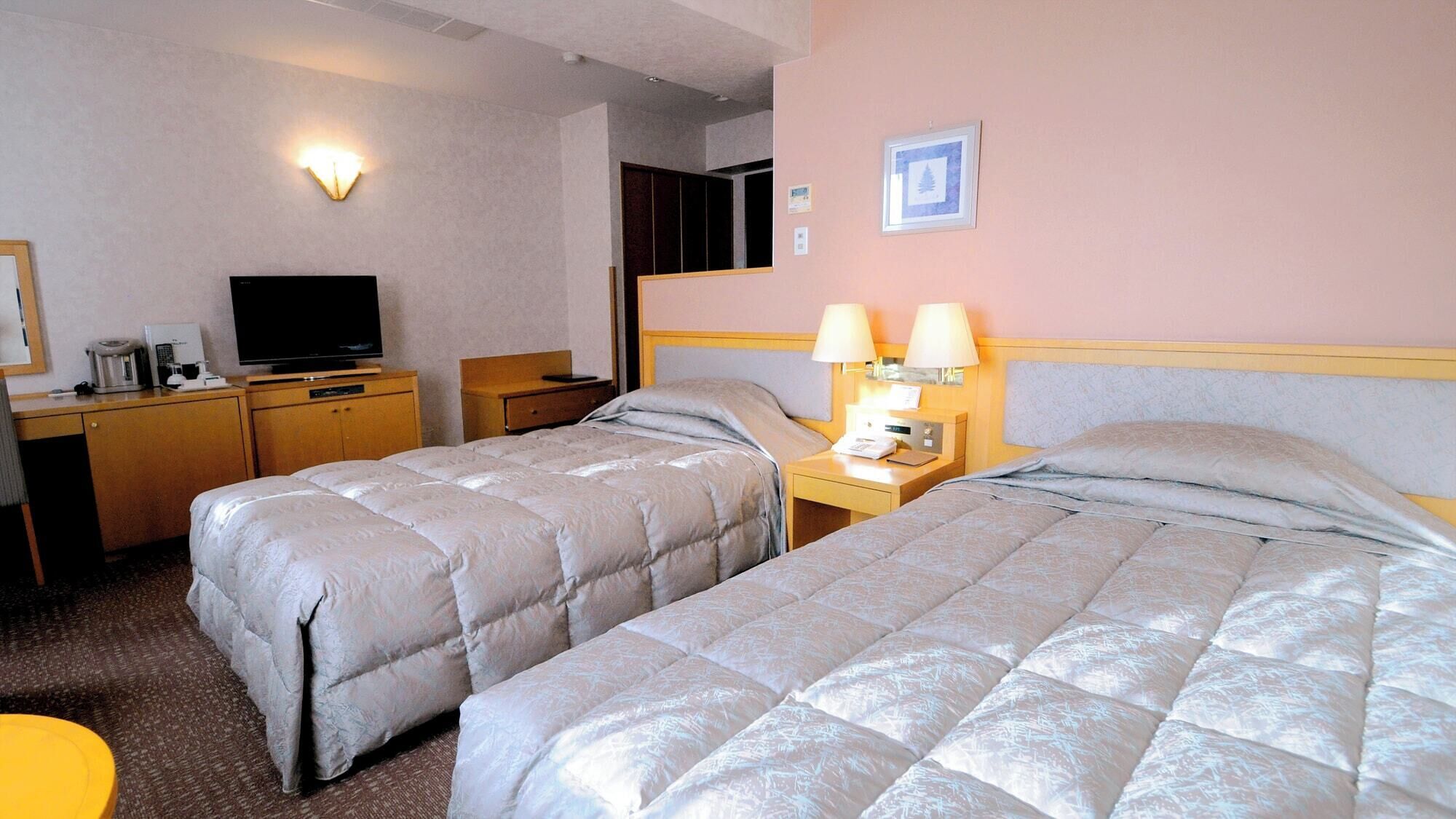 A hotel room with two beds, a desk with a TV, and a lamp.