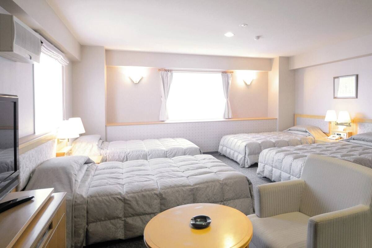 A hotel room with two beds, a TV, a desk, and a small table.