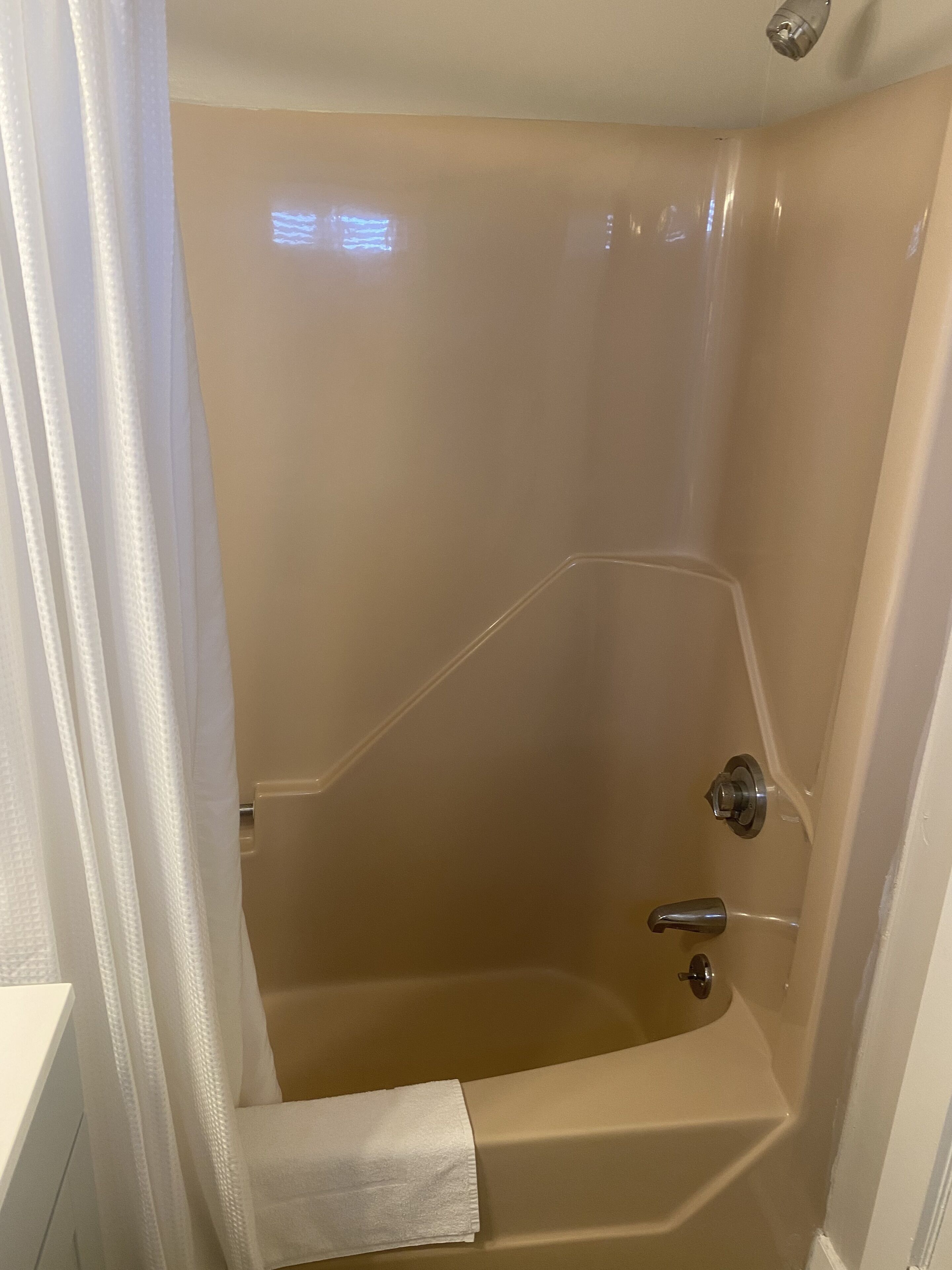 A small, beige-tiled bathroom with a shower, a white towel, and a shower curtain.