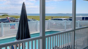 A pool area with a view of the ocean, a white fence, and parked cars. - On the Beach Motel (Old Orchard Beach)