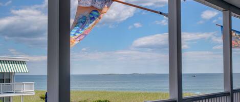 A covered porch with a view of the ocean and a distant island.