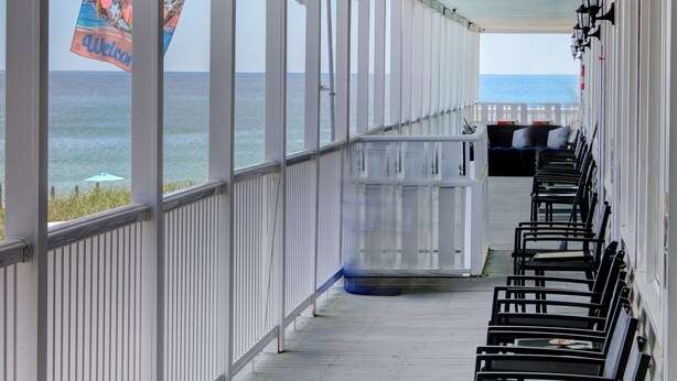 A covered walkway with rows of black chairs, a white railing, and a view of the ocean. - On the Beach Motel (Old Orchard Beach)