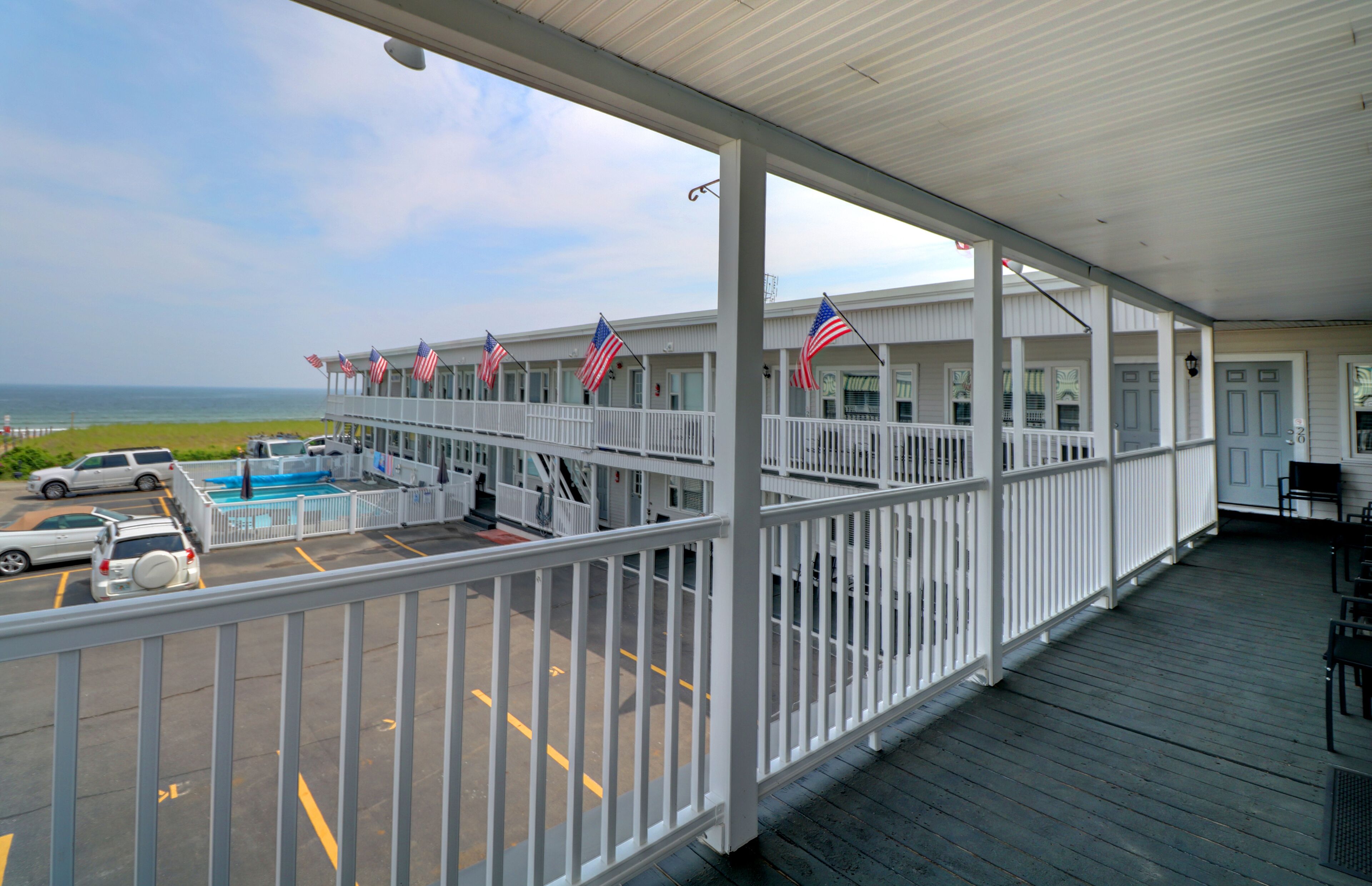 A covered outdoor area with a pool, American flags, and a view of the ocean.