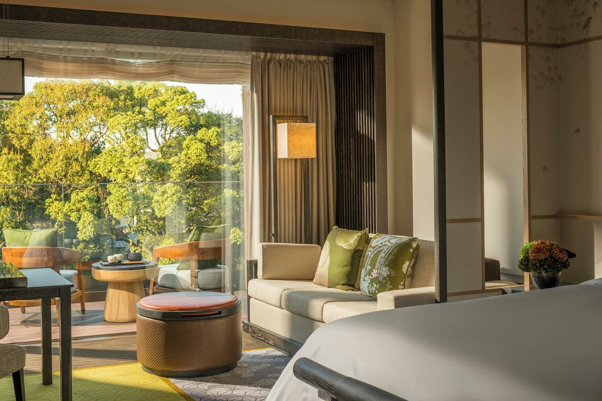 Ein modernes Hotelzimmer mit großem Fenster, einer Couch, einem Sessel, einem kleinen Tisch und einem Bett.