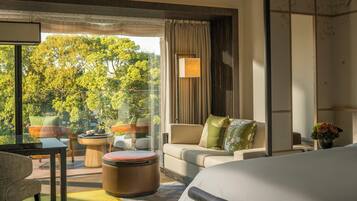 A modern hotel room with a large window, a sofa, a chair, a small table, and a bed.