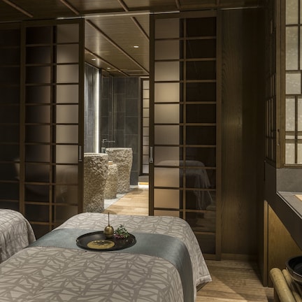 A modern hotel room with two beds, a wooden partition, and a view of a traditional Japanese garden.