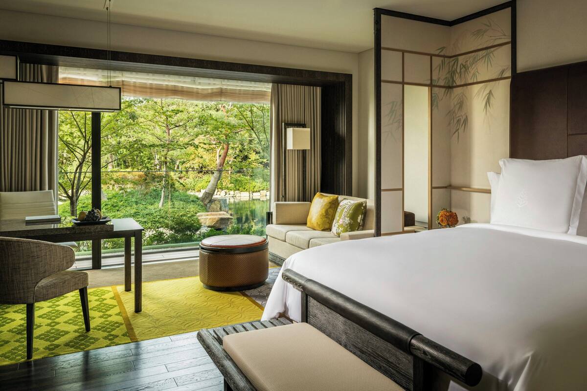 Ein Hotelzimmer mit einem großen Bett, einer Sitzecke, einem Esstisch und Blick auf Grünflächen.