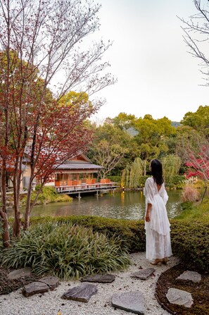 A woman in a white dress standing by a pond with a traditional building in the background.
