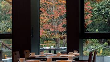 A dining area with tables set for a meal, overlooking a garden with autumn foliage.