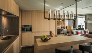 A modern kitchen with wooden cabinets, stainless steel appliances, and a central island with a bowl of fruit.