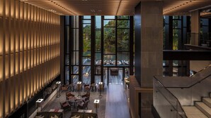 Eine großzügige Lobby mit hohen Decken, großen Fenstern mit Blick auf ein bewaldetes Gebiet und einer zentral gelegenen Sitzgelegenheit mit Tischen und Stühlen.