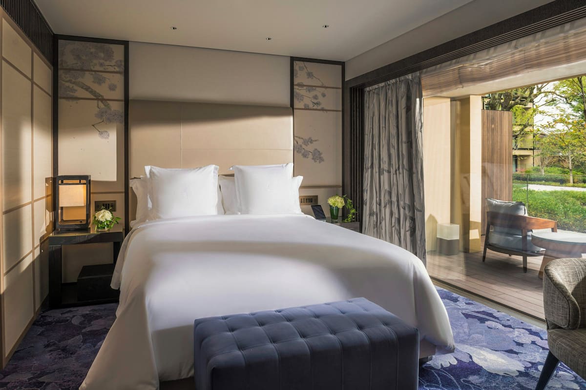 Ein modernes Hotelzimmer mit einem großen Bett, einer Sitzecke mit Sessel und Tisch und Blick ins Freie.