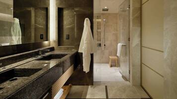 A modern bathroom with a large mirror, a granite sink, a shower, and a wooden stool.