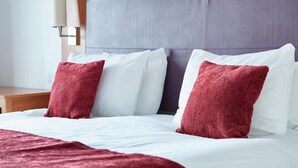A neatly made bed with white and red pillows, a purple headboard, and a wooden nightstand with a lamp. - Wheatsheaf Hotel by Chef and Brewer Collection (Basingstoke)
