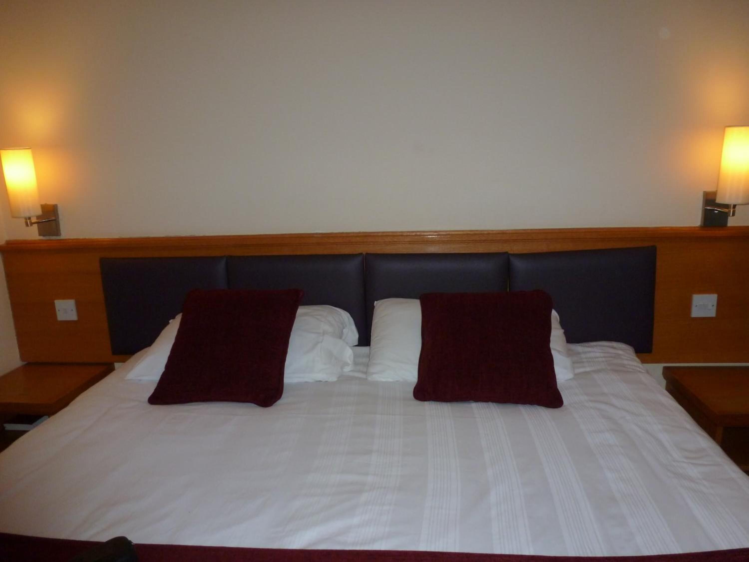 A hotel room with a large bed, two pillows, and two bedside lamps.