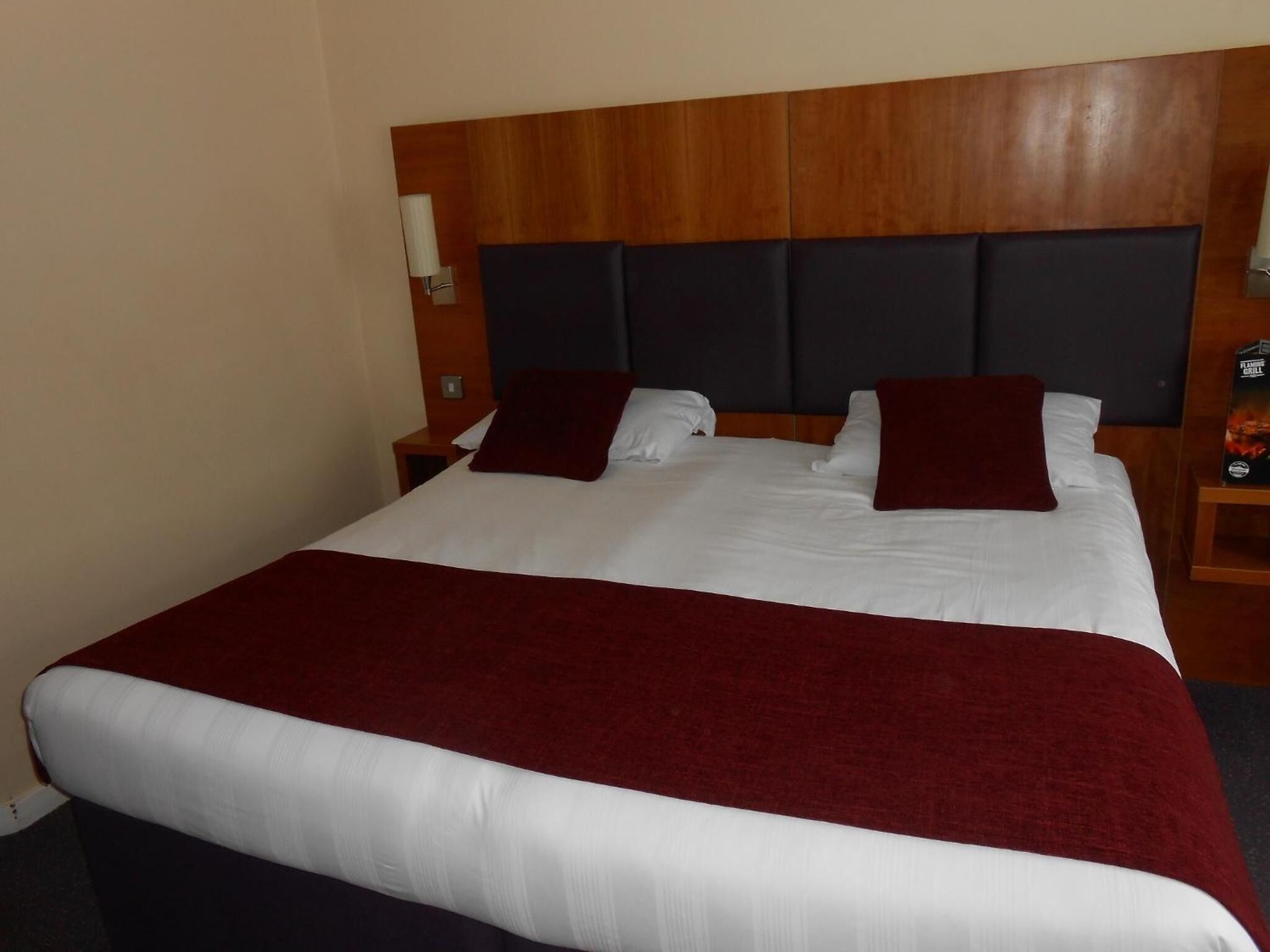 A hotel room with a large bed, wooden headboard, white bedding, and a red throw blanket.