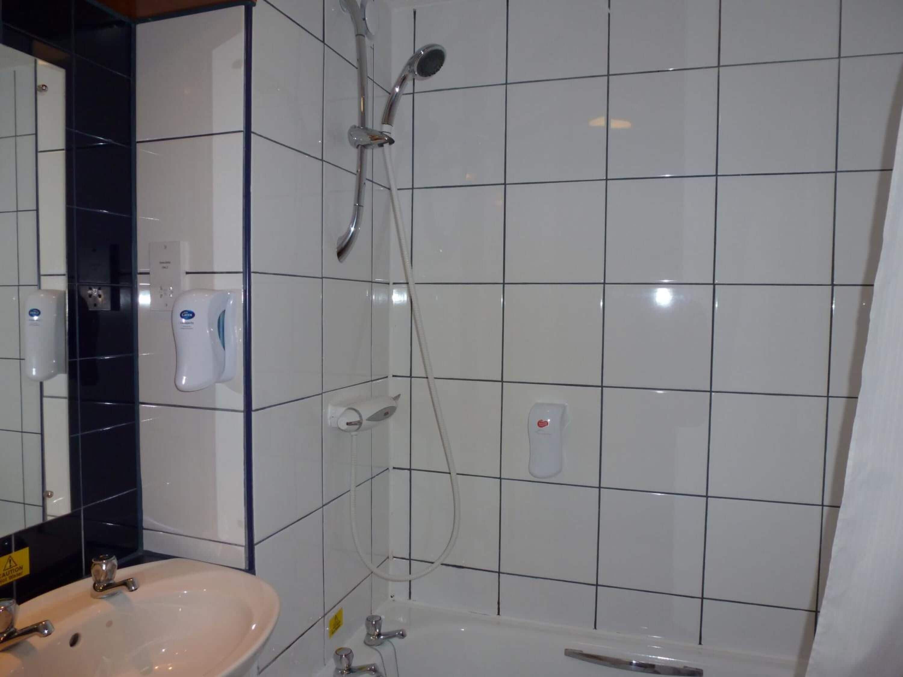 A bathroom with a sink, mirror, and a shower with a handheld showerhead.