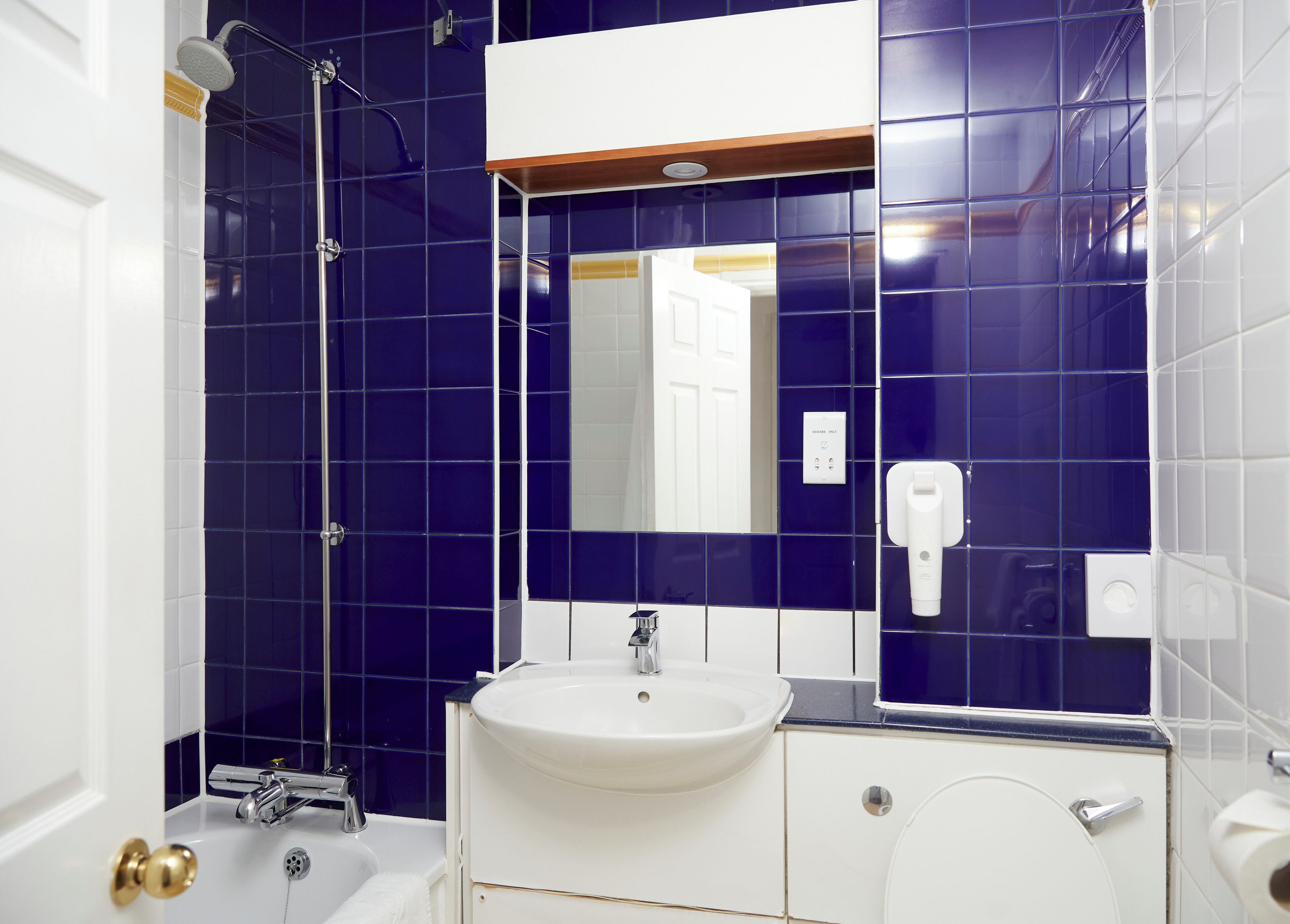A bathroom with a white sink, a mirror, a handheld showerhead, and a toilet.
