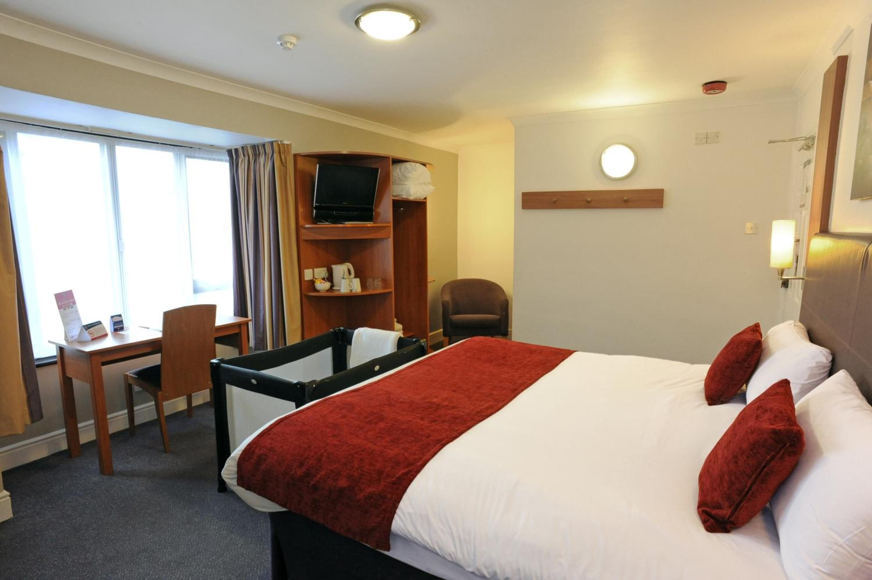 A hotel room with a bed, a desk, a chair, a TV, and a window with curtains.