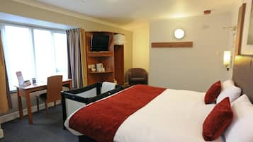 A hotel room with a bed, a desk, a chair, a TV, and a window with curtains.