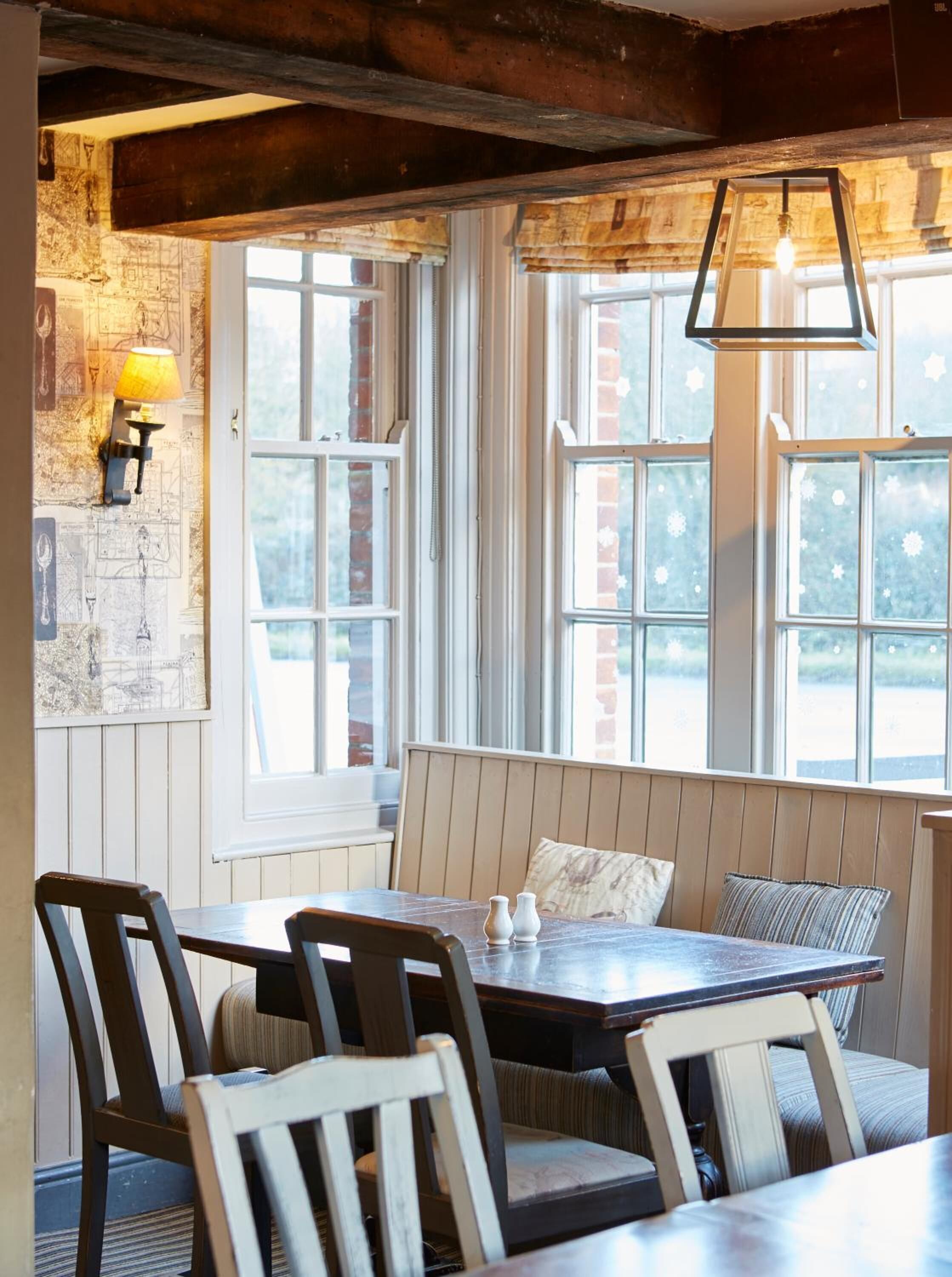 A dining area with a wooden table and chairs, a bench with cushions, and a window with a view of the outside.