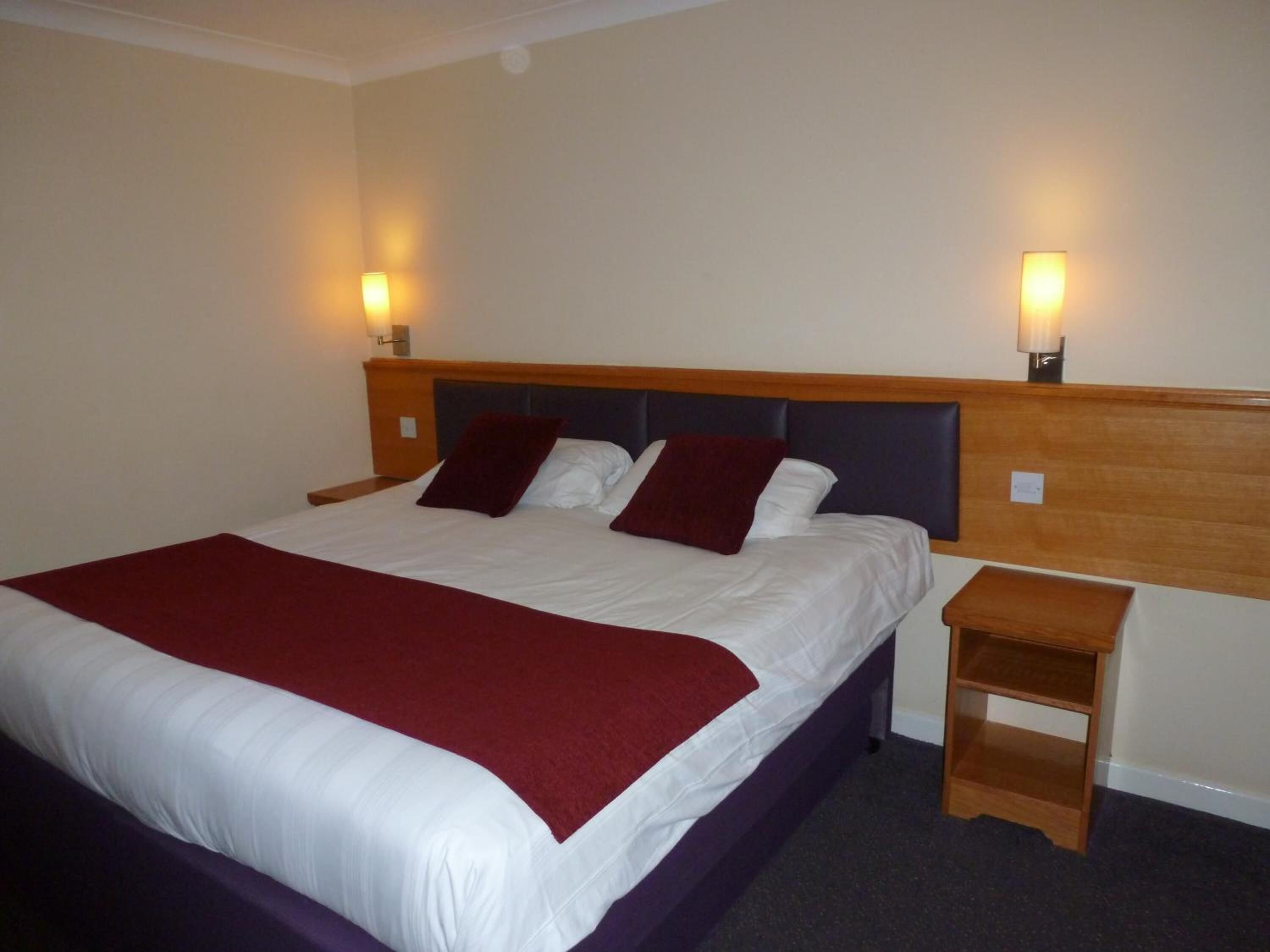 Una habitación de hotel con una cama grande, dos mesitas de noche y lámparas fijadas a la pared.