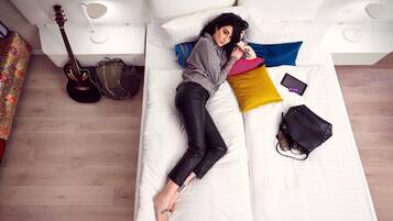 A bed with a guitar, a handbag, and a smartphone on it.